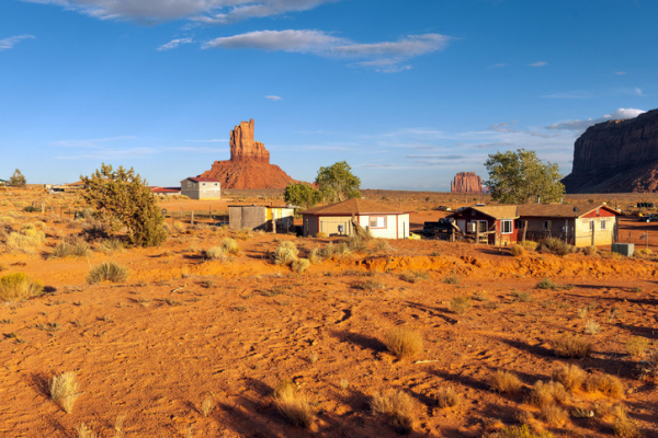 A scattering of housing on American Indian tribal land in Monument Valley; blue skies with fluffy clouds and red rocks in background